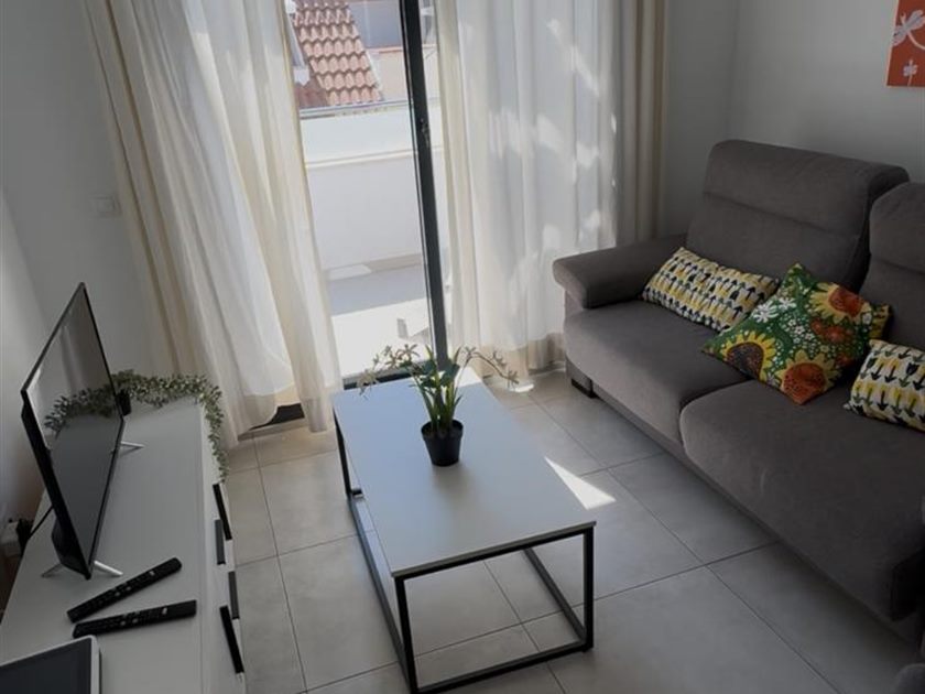 Salón de un apartamento turístico con sofá, mesa de centro y terraza al fondo